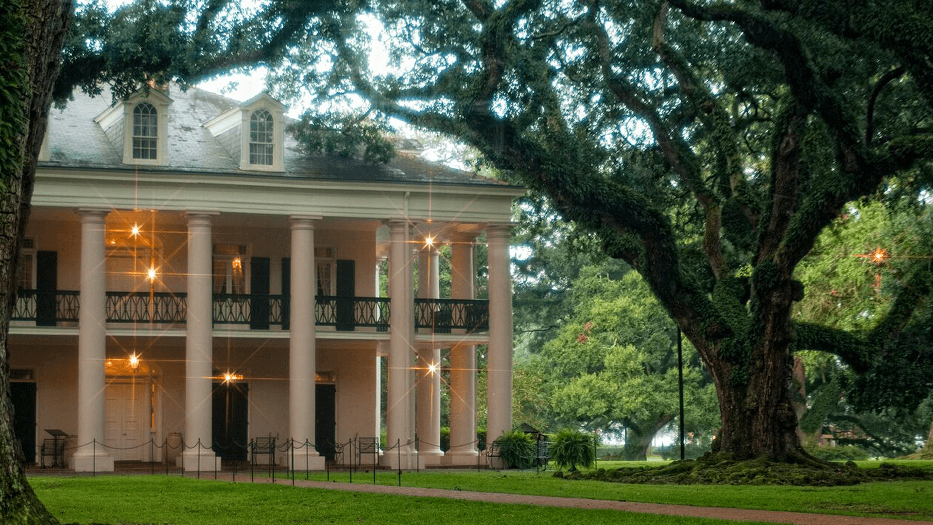 A stately pink mansion surrounded by lush greenery and large trees.
