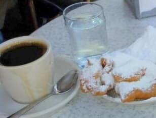 A cup of black coffee, a glass of water, and powdered sugar-dusted pastries on a plate.