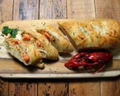 A platter of stuffed bread and a crawfish, garnished with herbs.