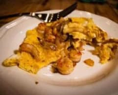 A partially eaten shrimp omelette on a white plate with a fork.