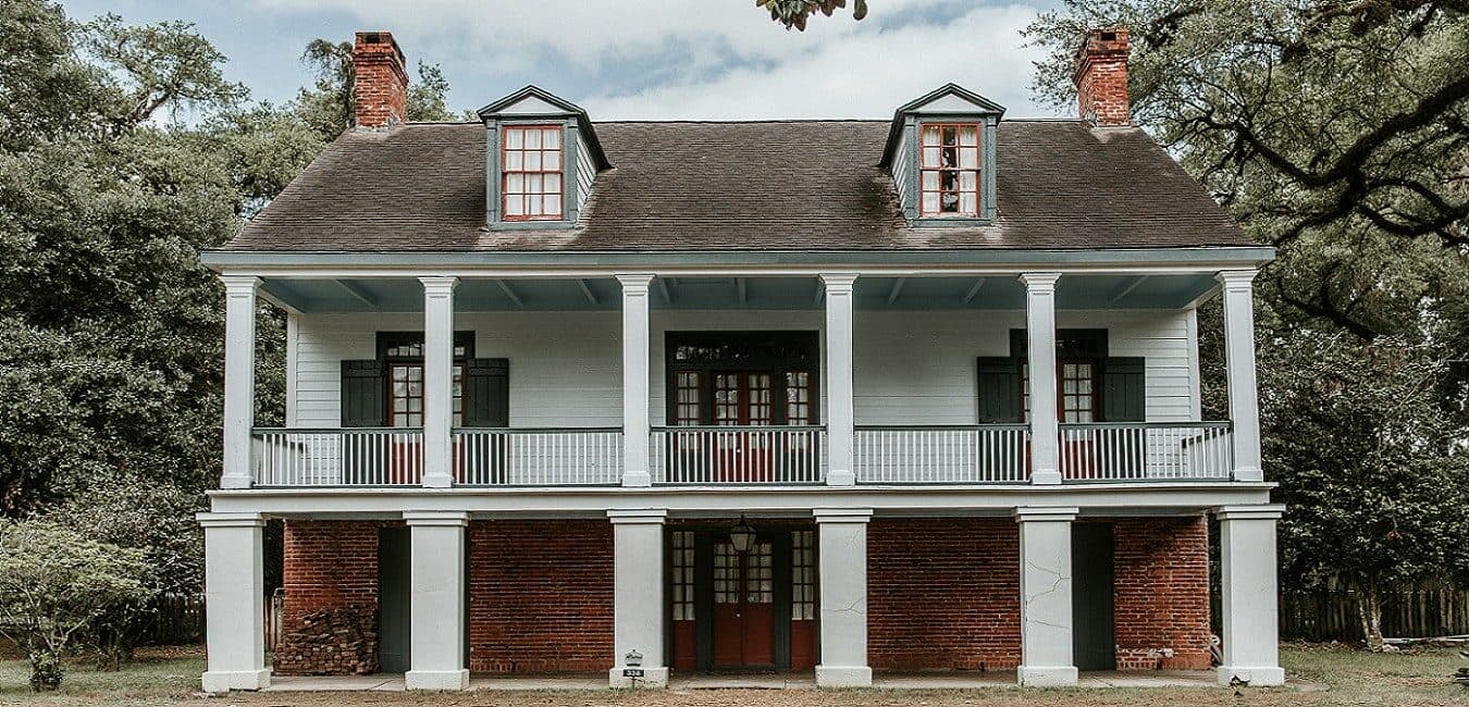 Historic two-story house featuring a front porch with columns and a mix of brick and wood siding.