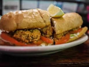 A toasted sandwich filled with fried oysters, lettuce, and tomato, garnished with a lemon wedge.